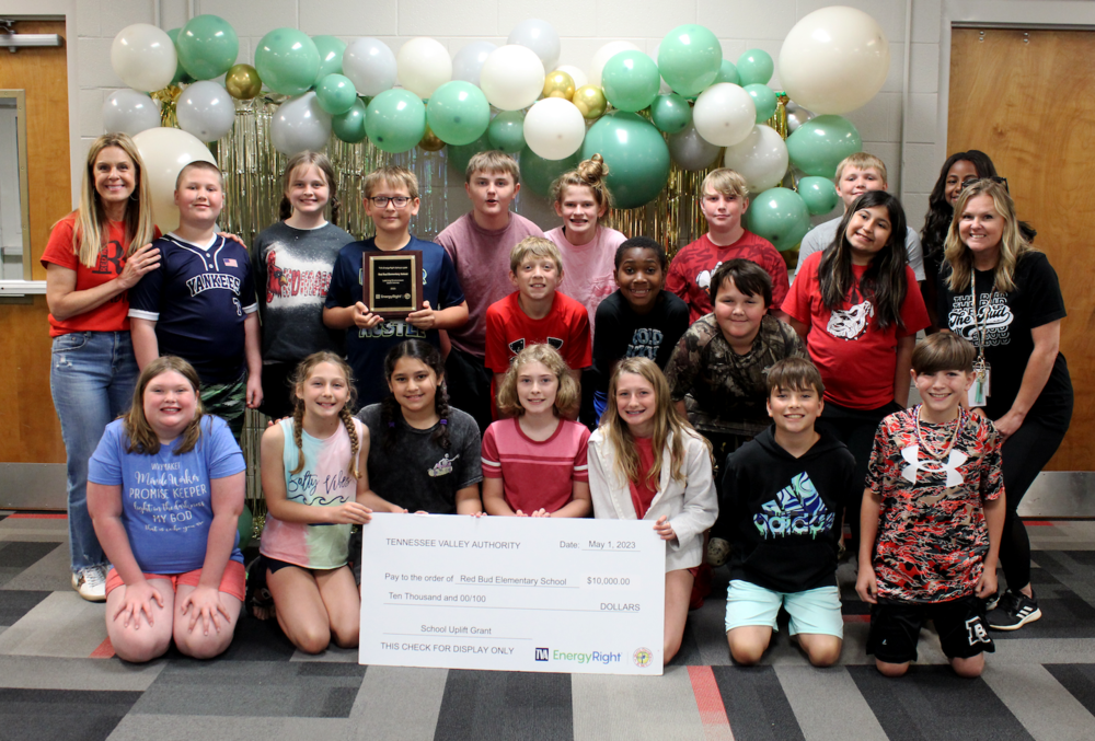 A group of RBES students stand together with a large check and a plaque