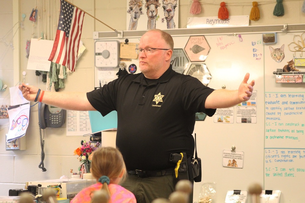 a police officer speaks to a class with his arms wide open