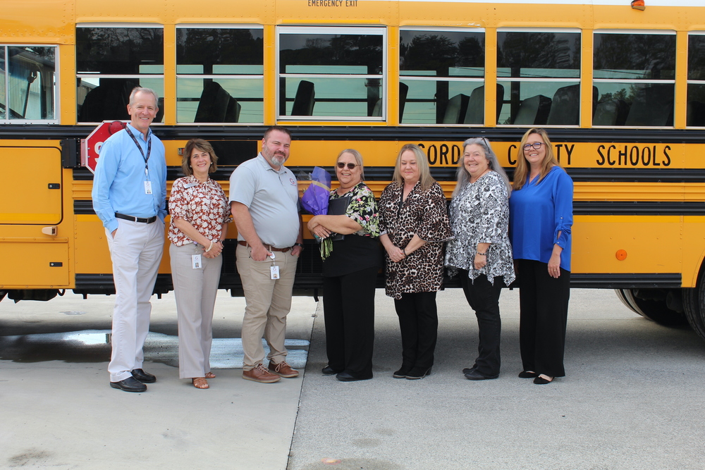 A group of adults stand together in front of a school bus