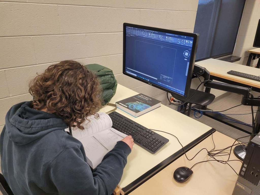 student looking at a book in front of a computer