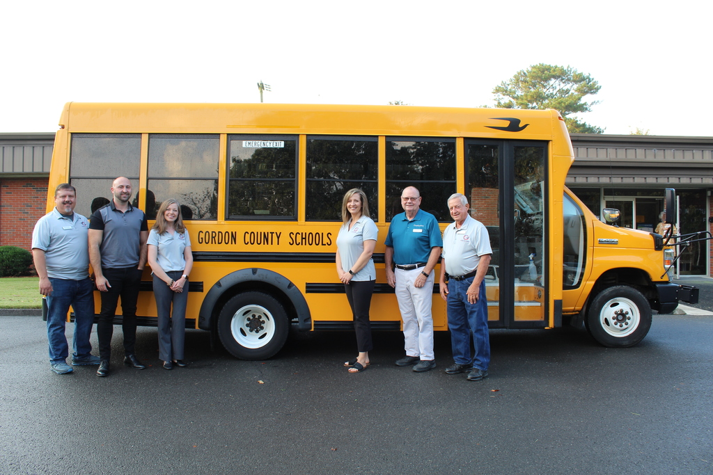 A group of adults stand in front of a bus 