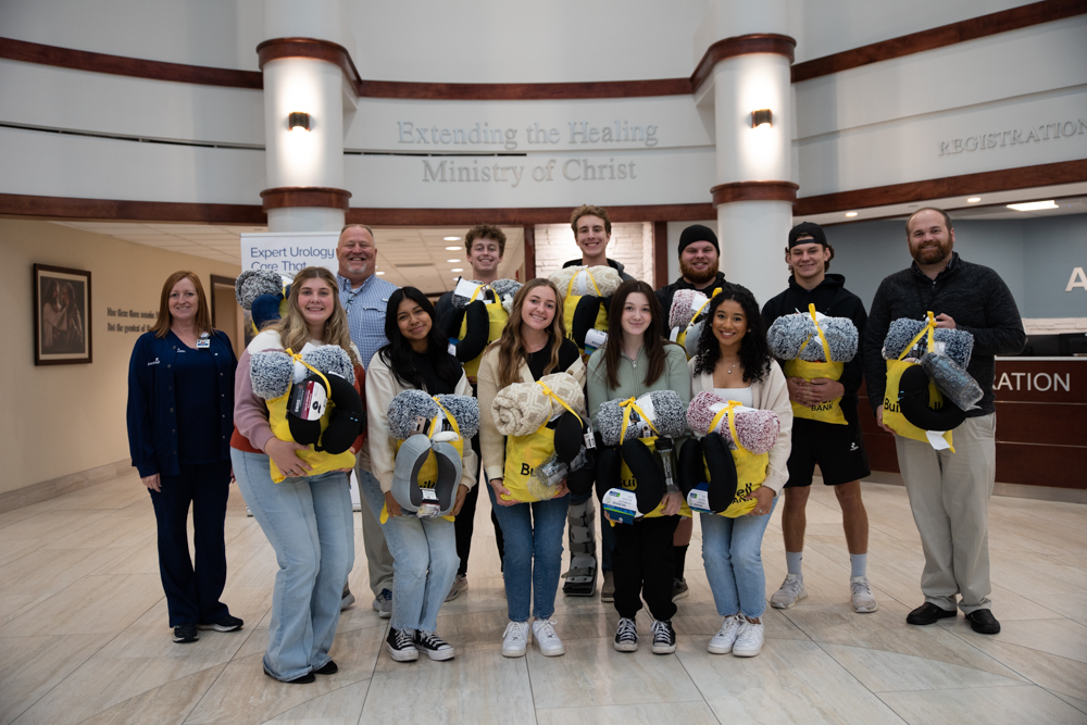 A group of students and adults stand together with cancer patient bags 