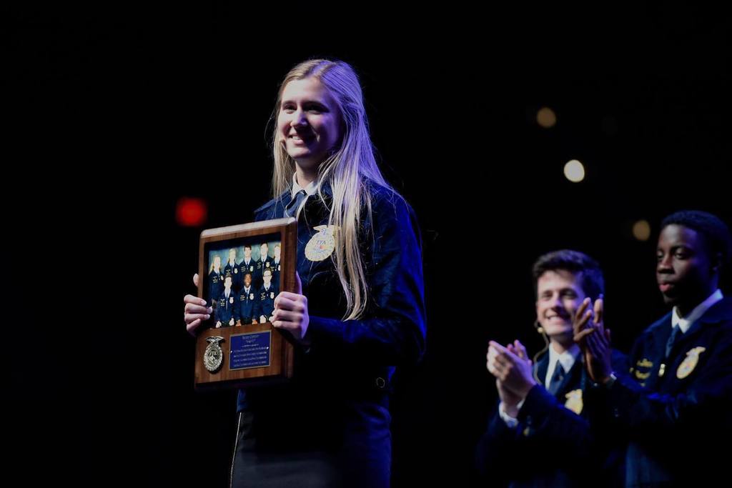 A STUDENT STANDS HOLDING HER PLAQUE