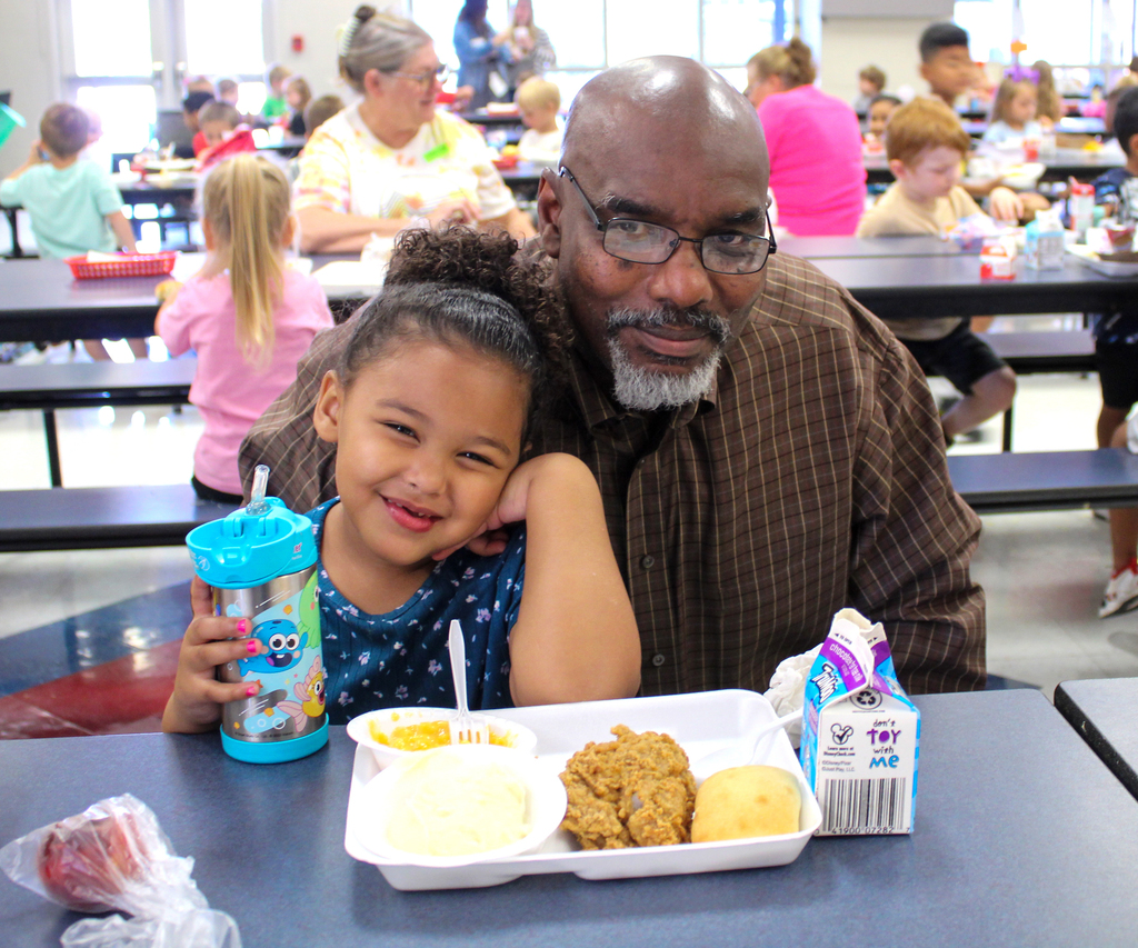 a man smiles with his granddaughter in front of a lunch tray