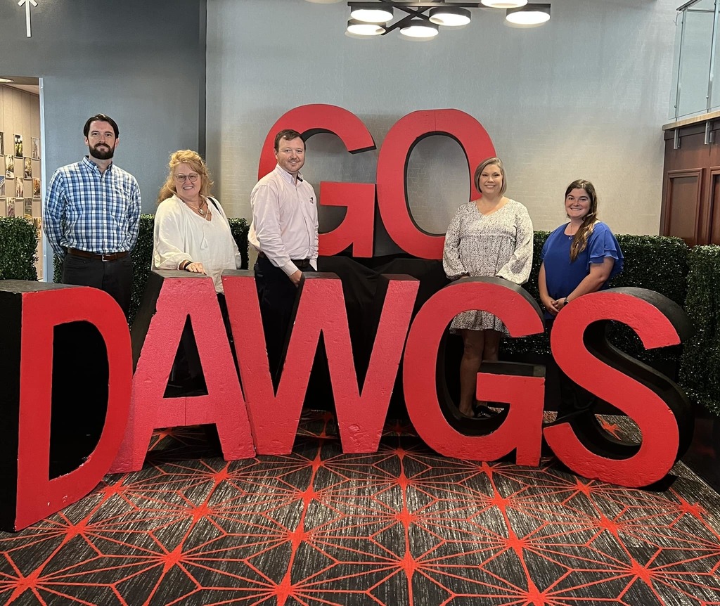 a group of adults stand together by a sign that says "go dawgs"